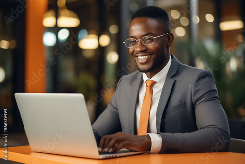 Happy successful African young businessman working on a laptop, black entrepreneur sitting in a cafe