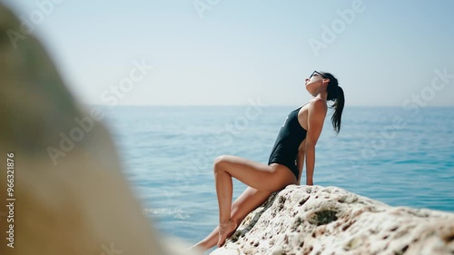 A woman is relaxing on a beach rock, enjoying the stunning ocean backdrop and scenery