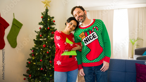 Loving couple embraces in tacky christmas sweaters next to the christmas tree at home