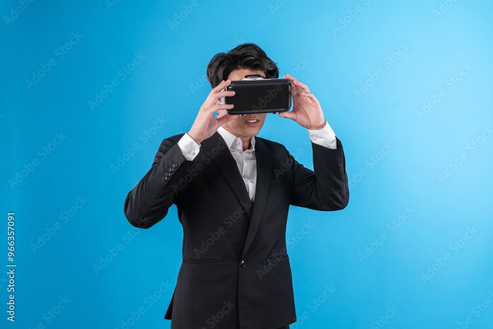 Smiling Asian businessman looking thorough VR connecting to business world report in futuristic metaverse, analyzing innovation technology ads in virtual reality isolated blue copyspace. Contrivance. Smiling Asian businessman looking thorough VR connecting to business world report in futuristic metaverse, analyzing innovation technology ads in virtual reality isolated blue copyspace. Contrivance.