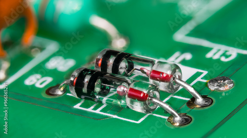 Two point-contact diodes in glass package on green printed circuit board. Closeup of electronic components with germanium crystal and metal wire semiconductor junction in striped tube on a PCB detail.
