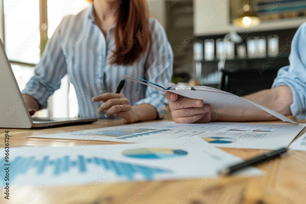 Two people are writing on a table with graphs and a laptop, generative ai image Two people are writing on a table with graphs and a laptop, generative ai image