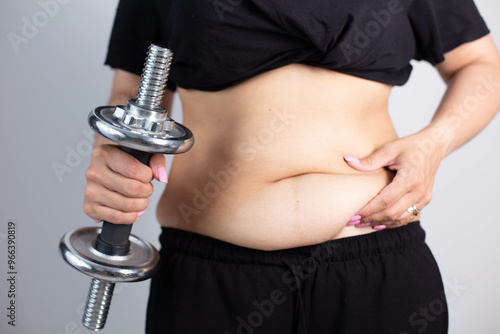 Woman cropped torso with sagging and bloated belly on grey background.