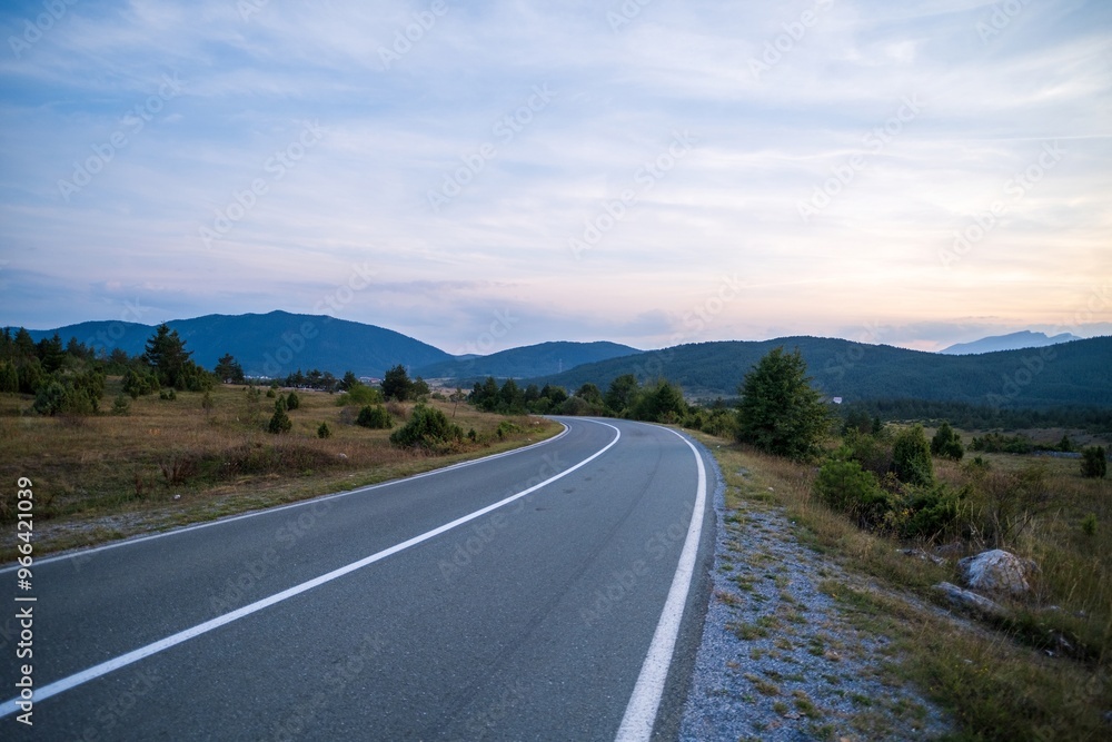 Winding rural road through open landscape at sunset Winding rural road through open landscape at sunset