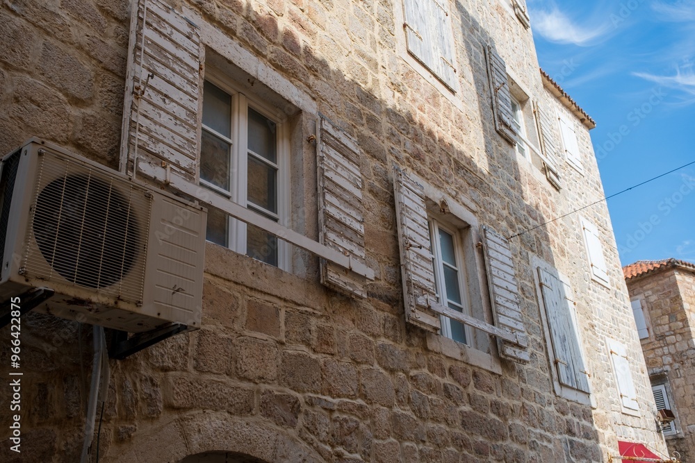 Fototapeta premium Old stone building with weathered shutters and AC unit