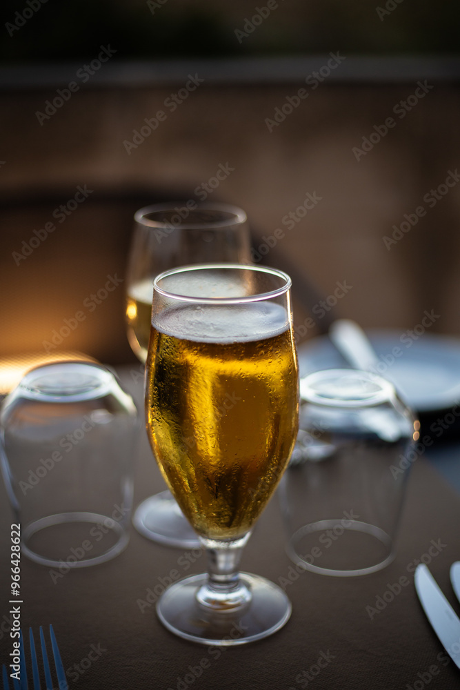 Blond golden beer served in a drinking glass on a served silverware table on brown palette, close up still Blond golden beer served in a drinking glass on a served silverware table on brown palette, close up still