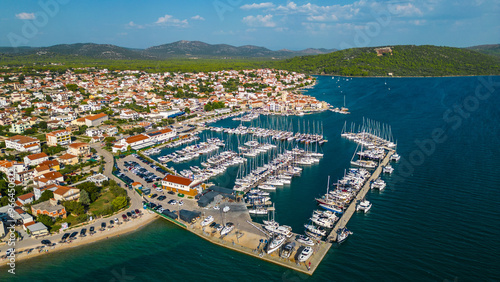 An aerial view of Pirovac Marina in Croatia, showcasing a stunning collection of yachts docked along the beautiful Adriatic coastline. The marina, surrounded by crystal-clear waters and picturesque 