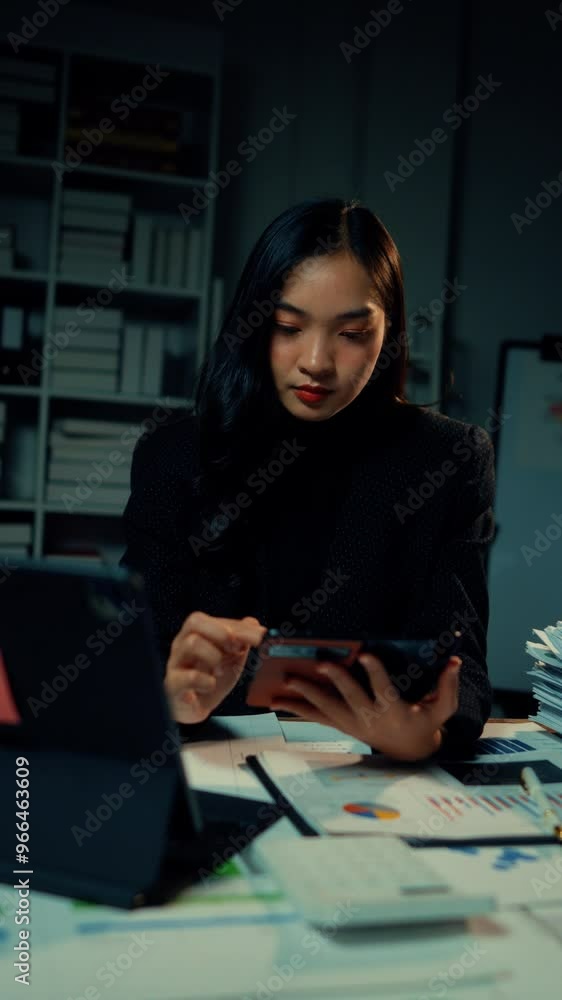 Young businesswoman works late in her office, using a calculator app on her smartphone to analyze figures and manage financial data with focus and determination Young businesswoman works late in her office, using a calculator app on her smartphone to analyze figures and manage financial data with focus and determination