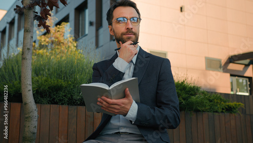 Thoughtful pensive man Caucasian businessman business coach in city write notes in notebook university professor writer thinking writing ideas at paper notepad smiling prepare for class lesson outside photo