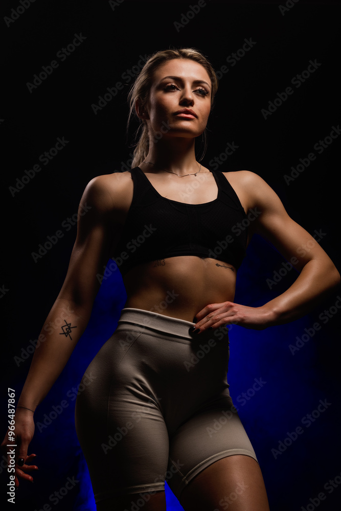 Confident athletic woman posing in gym wear with a determined expression, showcasing strength and empowerment against a dark background Confident athletic woman posing in gym wear with a determined expression, showcasing strength and empowerment against a dark background