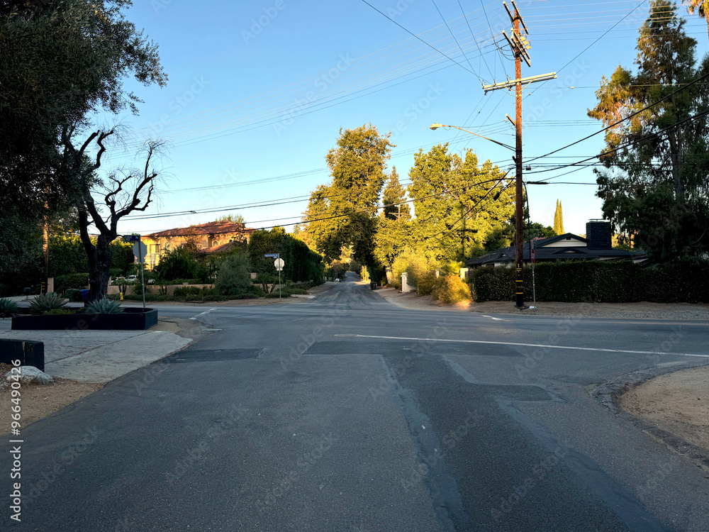 typical American neighborhood empty residential street intersection (driveways, homes, parked cars, telephone poles and wires, signs trees) beneath a bright blue summer sky in Los Angeles, California typical American neighborhood empty residential street intersection (driveways, homes, parked cars, telephone poles and wires, signs trees) beneath a bright blue summer sky in Los Angeles, California