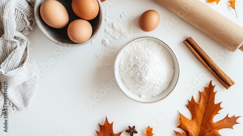 Bowls of flour and eggs on a white table with fall leaves, cinnamon sticks, and a rolling pin. Captures autumn baking charm, evoking warmth and comfort. Perfect for holiday prep or homemade dessert photo