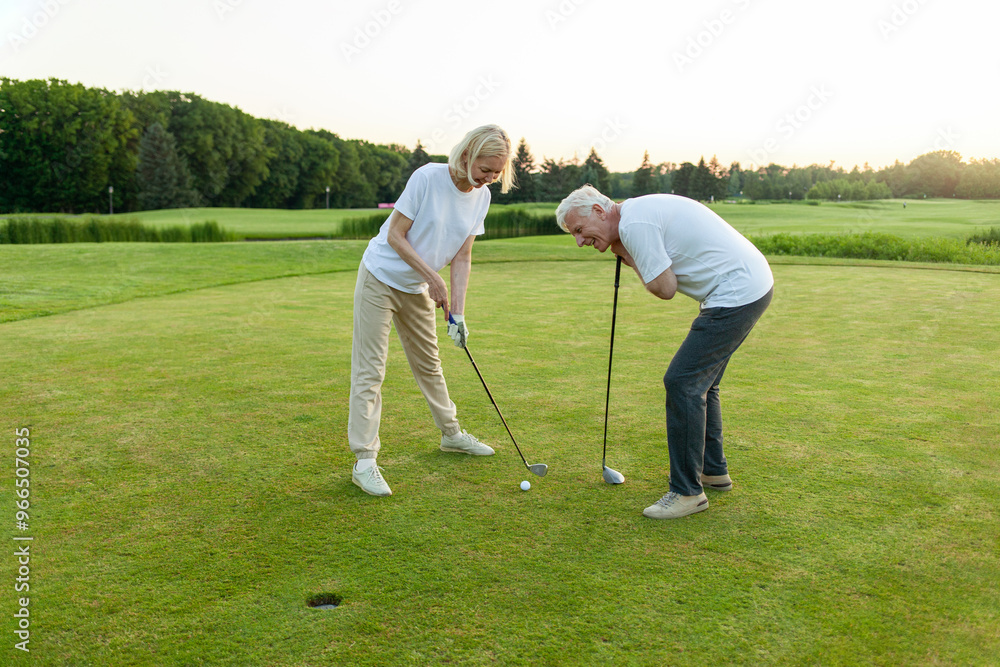 old senior couple in white clothes playing golf on golf course and chatting at sunset, elderly man and woman actively relaxing outdoors and laughing, pensioners on vacation old senior couple in white clothes playing golf on golf course and chatting at sunset, elderly man and woman actively relaxing outdoors and laughing, pensioners on vacation