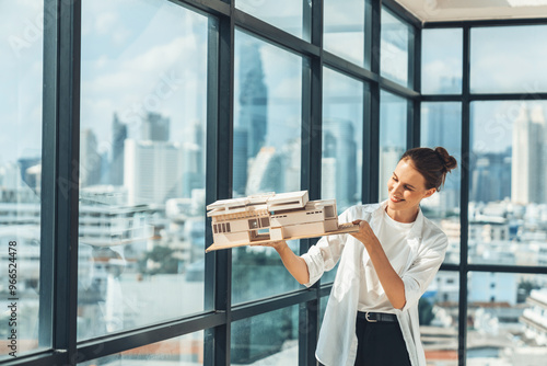 Young asian beautiful architect engineer raised house model while inspect carefully surrounded by city skyscraper view. Civil engineering, architectural studio. project planing. Tracery.