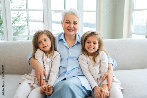 Happy family at home. Two little girls sisters twins grandmother enjoying time together. Good time at home. Grandma granddaughters child kids emotional bonding hugging together. Family generations