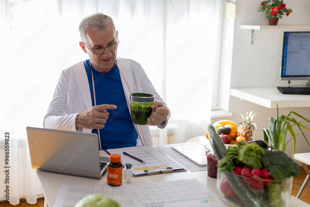 An experienced male nutritionist tells the patient about the benefits of a detox smoothie during an online session using a laptop. An experienced male nutritionist tells the patient about the benefits of a detox smoothie during an online session using a laptop.