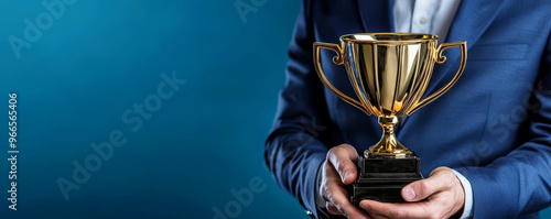 Businessman or boss holding champion golden trophy for winner, success and achievement award in business concept. Man in a suit with a gold trophy prize on blue background. photo