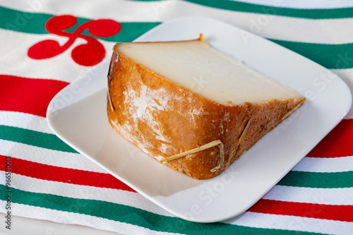 Piece of tasty Basque Brebis Fume smoked sheep cheese produced in south-western France, Northern Basque Country and towel with Basque symbol and colours photo