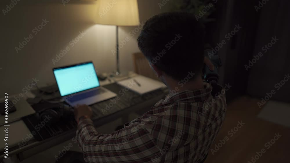 Cervical neck ache, nerve arthritis. Man studying late through night at laptop computer with cervical pain. Exhausted guy relaxing his neck using gun massager while overworking at notebook computer. Cervical neck ache, nerve arthritis. Man studying late through night at laptop computer with cervical pain. Exhausted guy relaxing his neck using gun massager while overworking at notebook computer.