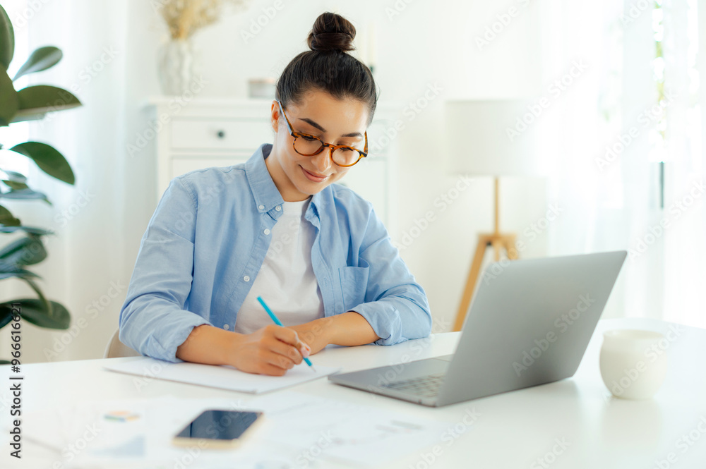 Focused successful arabian or indian brunette woman in a blue shirt, sitting at a work desk while working in the laptop, doing online tasks, develop new digital project, planning marketing strategy Focused successful arabian or indian brunette woman in a blue shirt, sitting at a work desk while working in the laptop, doing online tasks, develop new digital project, planning marketing strategy