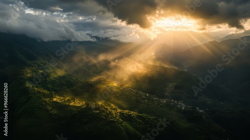 Dramatic sunlight breaks through clouds over a lush, mountainous landscape, casting a golden glow on the verdant valley below.