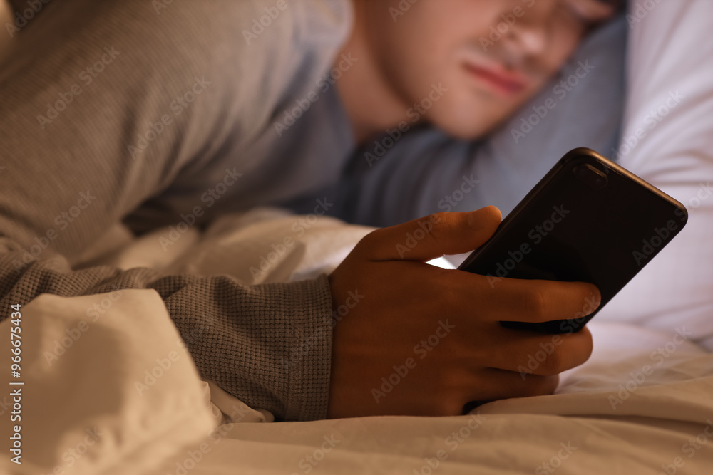 Young man with mobile phone sleeping in bed at night, closeup