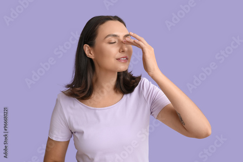 Young woman touching her nose on lilac background