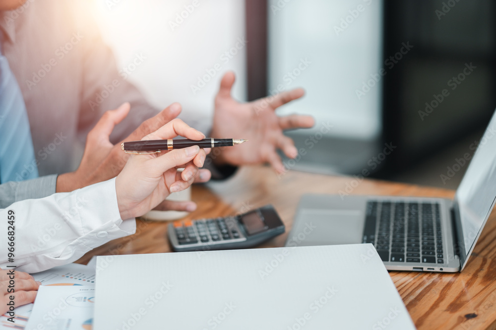 Fototapeta premium Close-up of hands during a business meeting, with a laptop, calculator, and documents on a wooden table in a modern office.