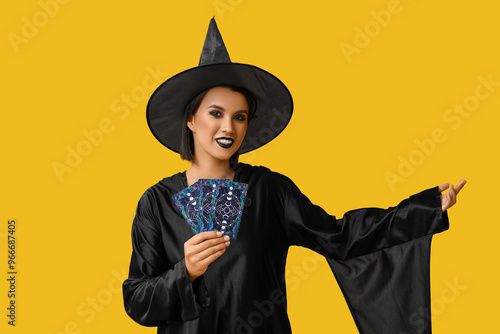 Beautiful young happy witch with tarot cards on yellow background