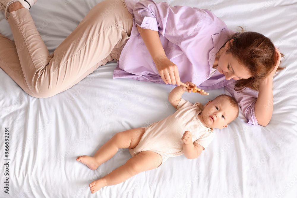 Beautiful young mother and cute little baby playing with rattle while lying in bedroom at home, top view Beautiful young mother and cute little baby playing with rattle while lying in bedroom at home, top view