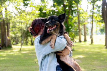 A woman holding her dog in her arms while walking through a green park, hugging her pet.