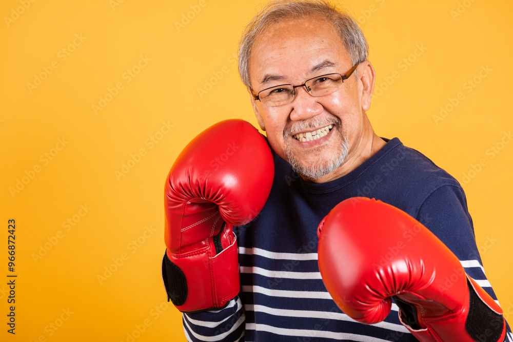 Portrait Asian old man wearing glasses wear two red boxing gloves studio shot isolated yellow background, smiling happy elderly man gray haired healthy fighter lifestyle concept Portrait Asian old man wearing glasses wear two red boxing gloves studio shot isolated yellow background, smiling happy elderly man gray haired healthy fighter lifestyle concept
