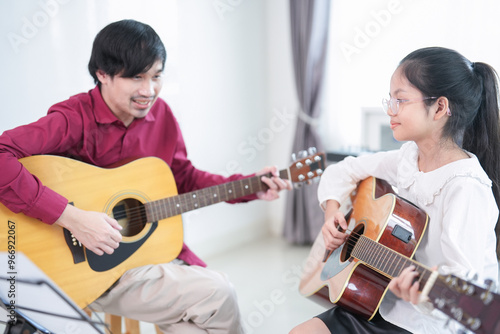 asian girl child playing guitar with teacher in the room,adult help kid to learn music,concept of music studying,music education,classical band photo