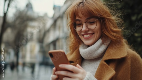 Young woman holding cellphone and smiling Caucasian female walking on street 