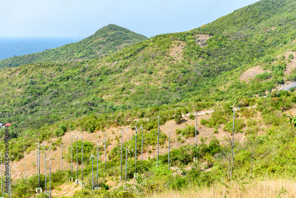 Fototapeta premium Wind power on the mountain and blue sea on a clear sky background morning day at Koh Larn island. View point on mountain to see view of windmill and sky. Wind turbine. Wind Energy. Pattaya, Thailand.