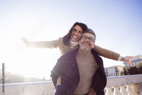 Elated middle-aged couple enjoys a carefree piggyback ride in a city on a sunny winter day