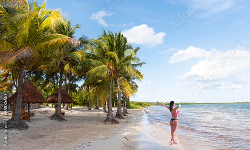 Happy slim girl in red and black bikini  with raised up arms on the seashore in Paradise Sunny beach with palms and turquoise sea. Summer vacation and tropical beach concept - Cancun, Mexico