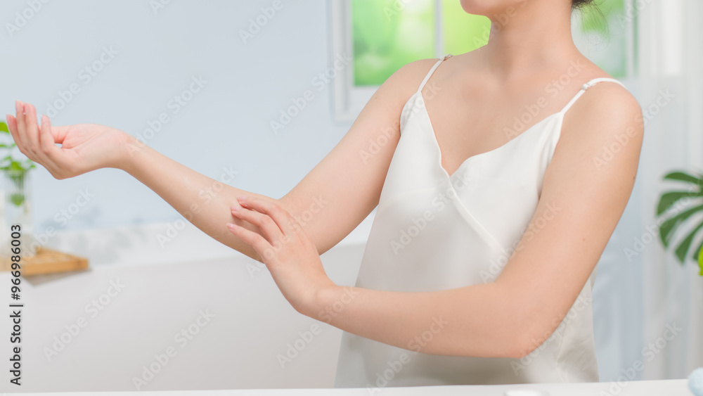 The bathroom background is bright with relaxing atmosphere featuring a woman applies lotion to her forearm, practicing a self-care routine. Suitable photo for skincare advertising. The bathroom background is bright with relaxing atmosphere featuring a woman applies lotion to her forearm, practicing a self-care routine. Suitable photo for skincare advertising.