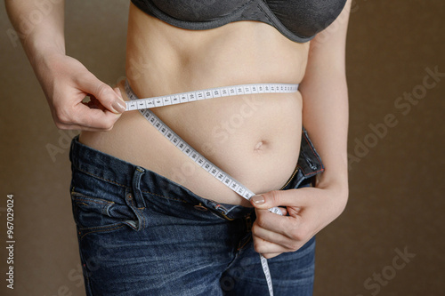 Woman carefully measures her waist with flexible tape measure to ensure accurate measurements for her clothing or medical purposes. Concept of excess weight, diet