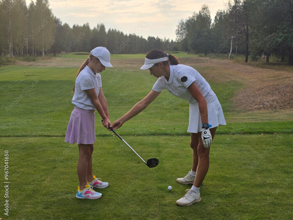 Obraz premium Young girl receives golf instruction on a course in a serene wooded landscape during late
