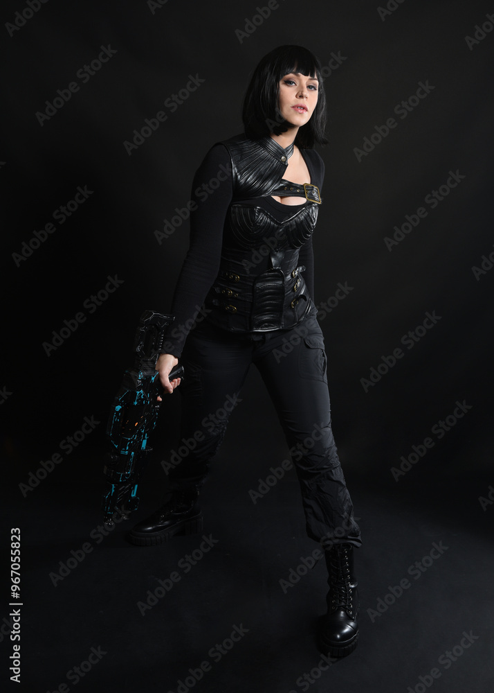 Full length portrait of beautiful black female model wearing sci fi futuristic dystopian leather bodysuit costume. Standing pose, holding gun weapon. isolated dark studio background moody silhouette. Full length portrait of beautiful black female model wearing sci fi futuristic dystopian leather bodysuit costume. Standing pose, holding gun weapon. isolated dark studio background moody silhouette.