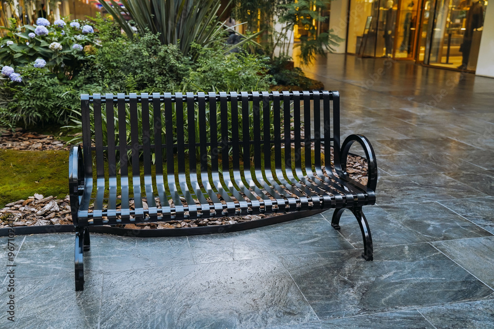 A wrought iron bench is placed in shopping mall for people to sit and rest.