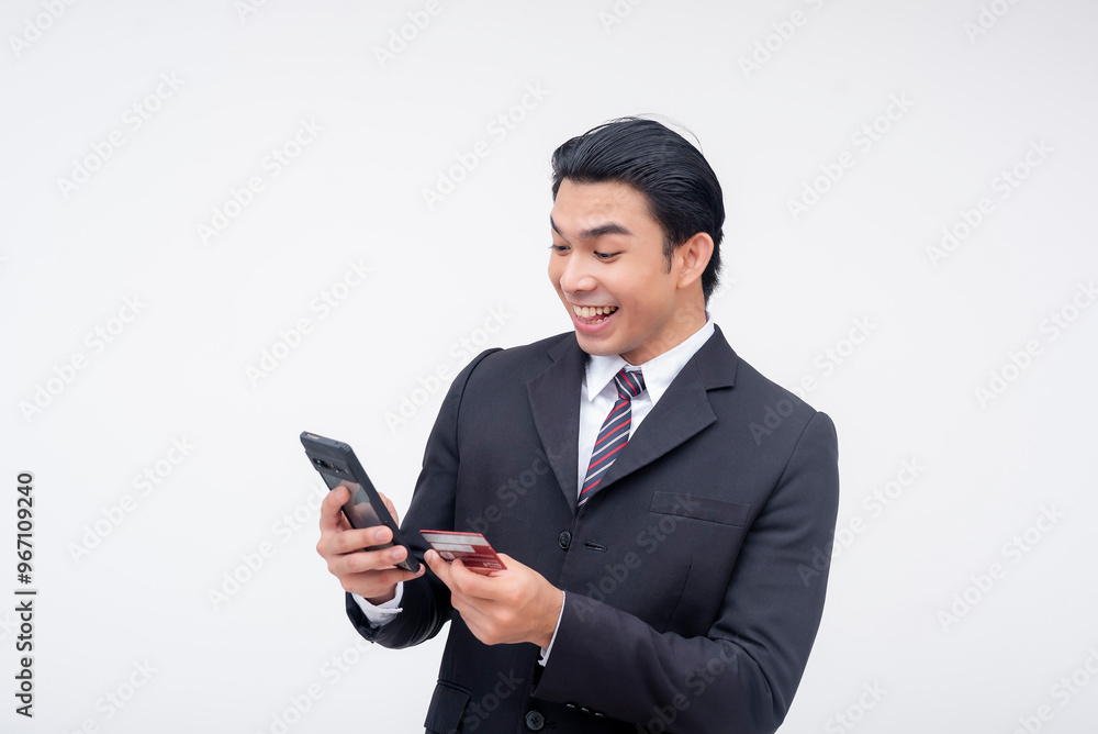 A young asian business executive elated to use this credit or debit card to purchase a product or service online on his phone. Online banking or fintech concept. Isolated on a white background. A young asian business executive elated to use this credit or debit card to purchase a product or service online on his phone. Online banking or fintech concept. Isolated on a white background.
