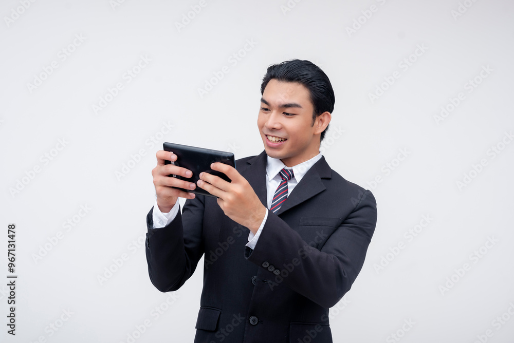 A young asian business executive smiling while playing a game on his phone, passing the time. Isolated on a white background. A young asian business executive smiling while playing a game on his phone, passing the time. Isolated on a white background.