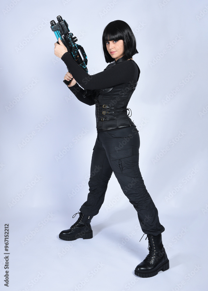 Full length portrait of beautiful black female model with short black hair wearing sci fi futuristic dystopian leather bodysuit costume. Standing pose holding gun weapon, isolated white studio backgro Full length portrait of beautiful black female model with short black hair wearing sci fi futuristic dystopian leather bodysuit costume. Standing pose holding gun weapon, isolated white studio backgro