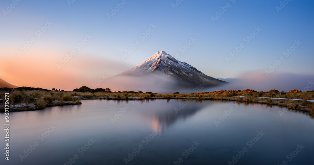Snow-capped Mt Taranaki reflected in the clear water of Pouakai tarn at Sunrise, New Zealand.