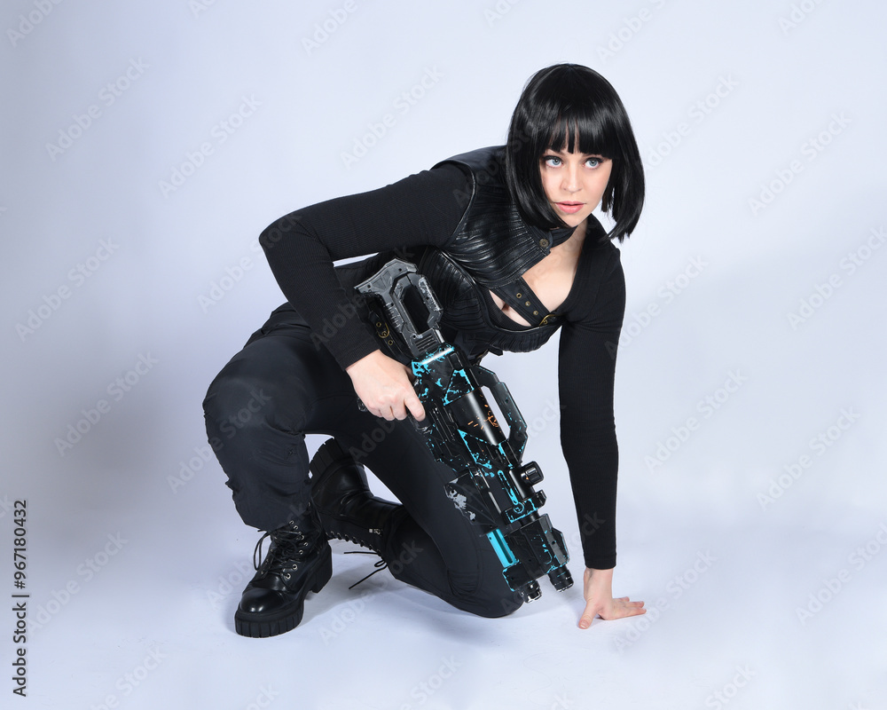 Full length portrait of beautiful black female model, black hair wearing sci fi futuristic dystopian leather bodysuit costume. sitting pose, holding gun weapon, isolated white studio background. Full length portrait of beautiful black female model, black hair wearing sci fi futuristic dystopian leather bodysuit costume. sitting pose, holding gun weapon, isolated white studio background.