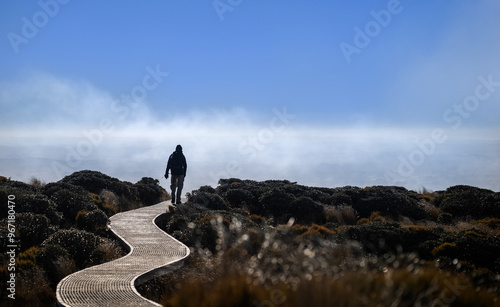Obraz na płótnie Man in silhouette hiking Pouakai circuit, walking on boardwalk. Views of the Taranaki in the mist. Egmont National park. New Zealand. w salonie