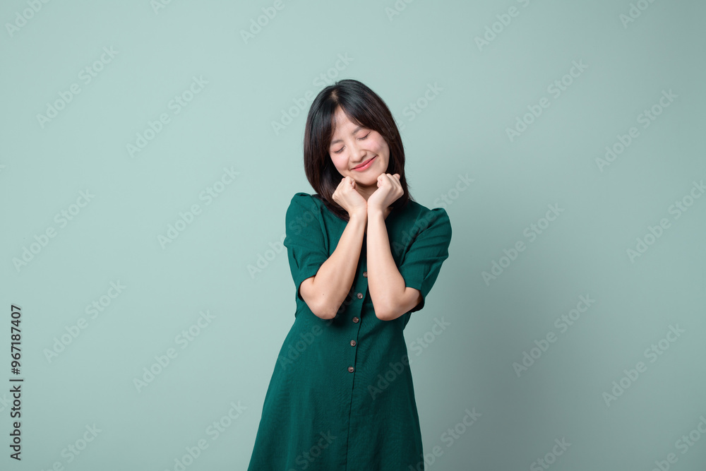 Adorable happy young asian woman model with shy emotion smiling expression cheerful positive attractive face and holding hand isolated on green pastel studio background. Portrait beautiful cute lady. Adorable happy young asian woman model with shy emotion smiling expression cheerful positive attractive face and holding hand isolated on green pastel studio background. Portrait beautiful cute lady.