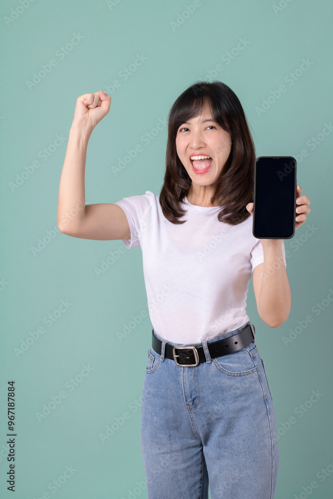 Woman in a white t-shirt smiling and holding a smartphone with a happy expression on a green background, showing satisfaction. Woman in a white t-shirt smiling and holding a smartphone with a happy expression on a green background, showing satisfaction.